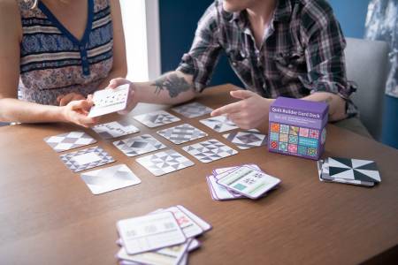 Two people using Quilt Builder Card Deck Set number 3 on a table to explore creative quilt block designs and layouts.