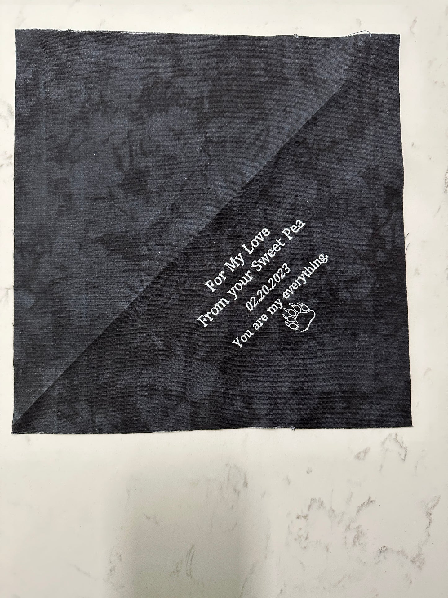 Custom embroidered quilt label with personalized message on dark cotton fabric, featuring a simple graphic design.