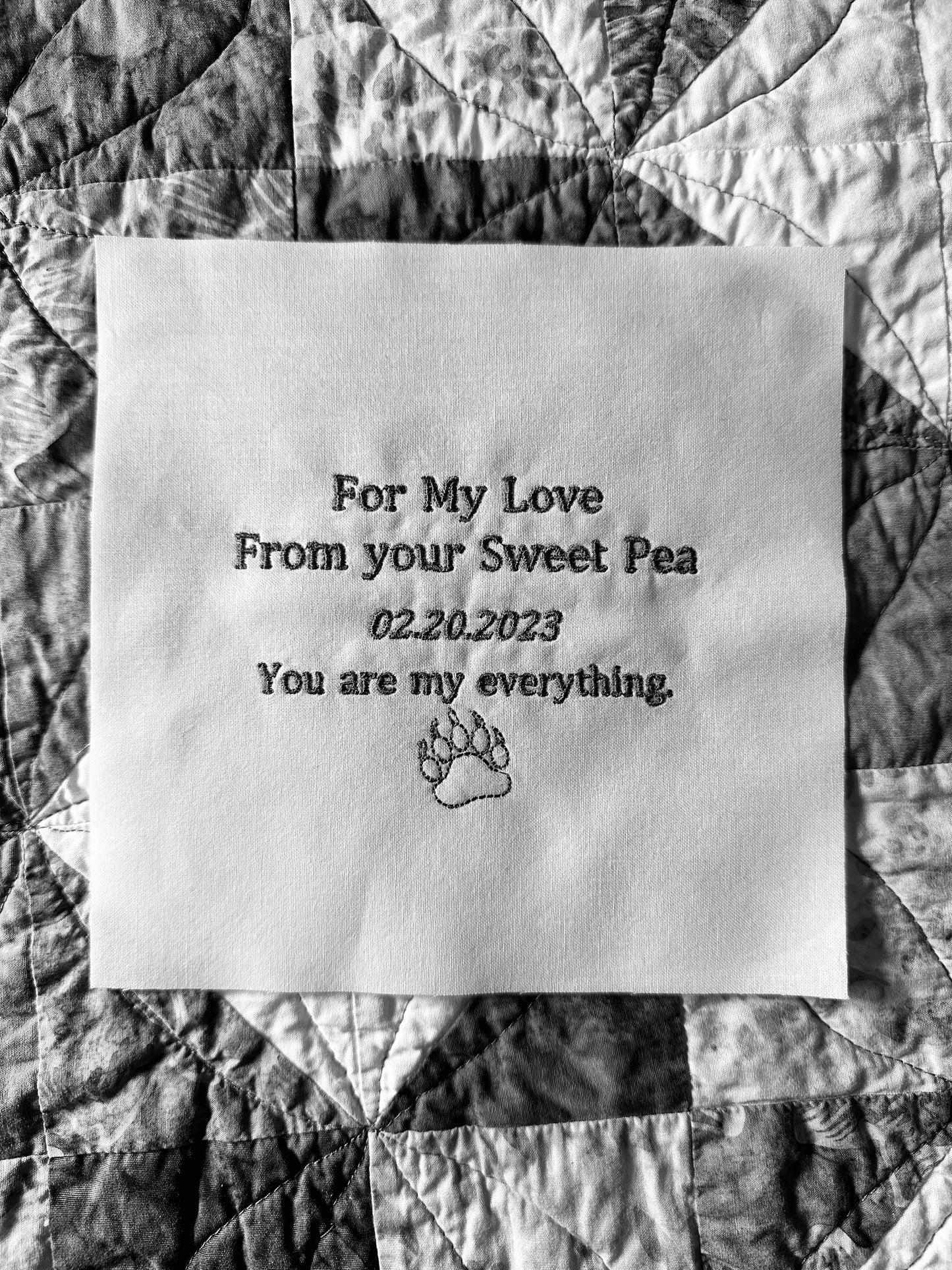 Customized embroidered quilt label with personal message and paw print graphic on quilt cotton.