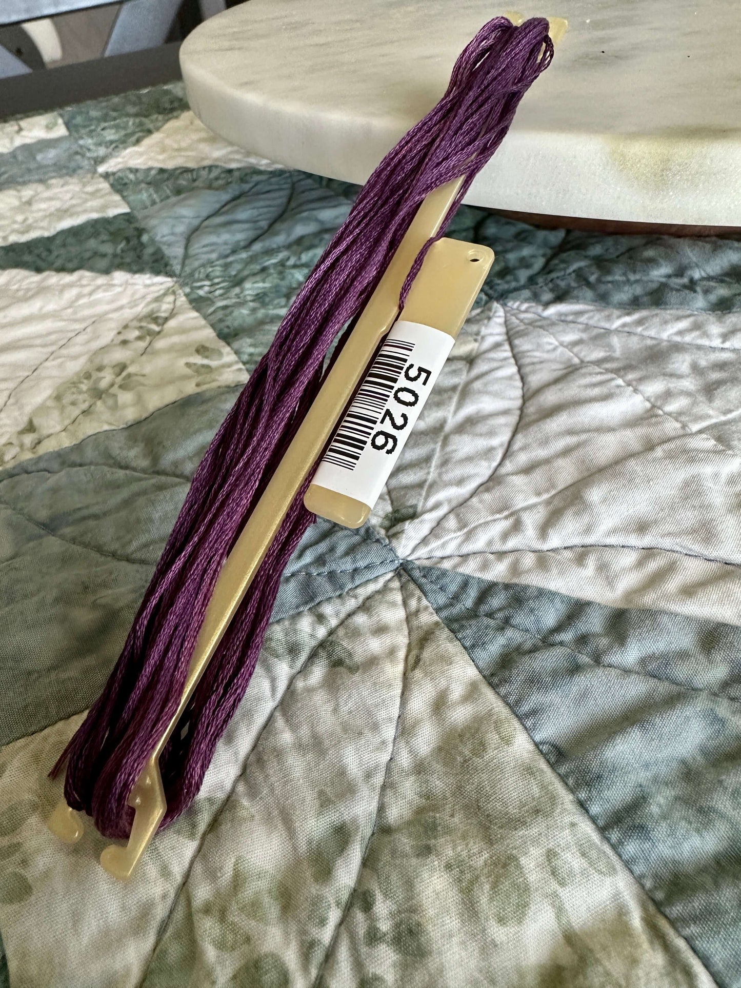 Stitchbow Floss Holder with purple embroidery floss on quilted fabric surface.