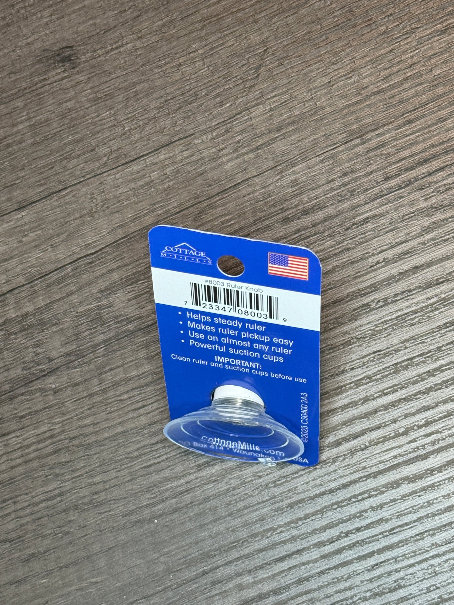 Ruler Knob Cottage Mills 8003 suction cup with blue packaging on wooden surface for easy ruler pickup and placement.