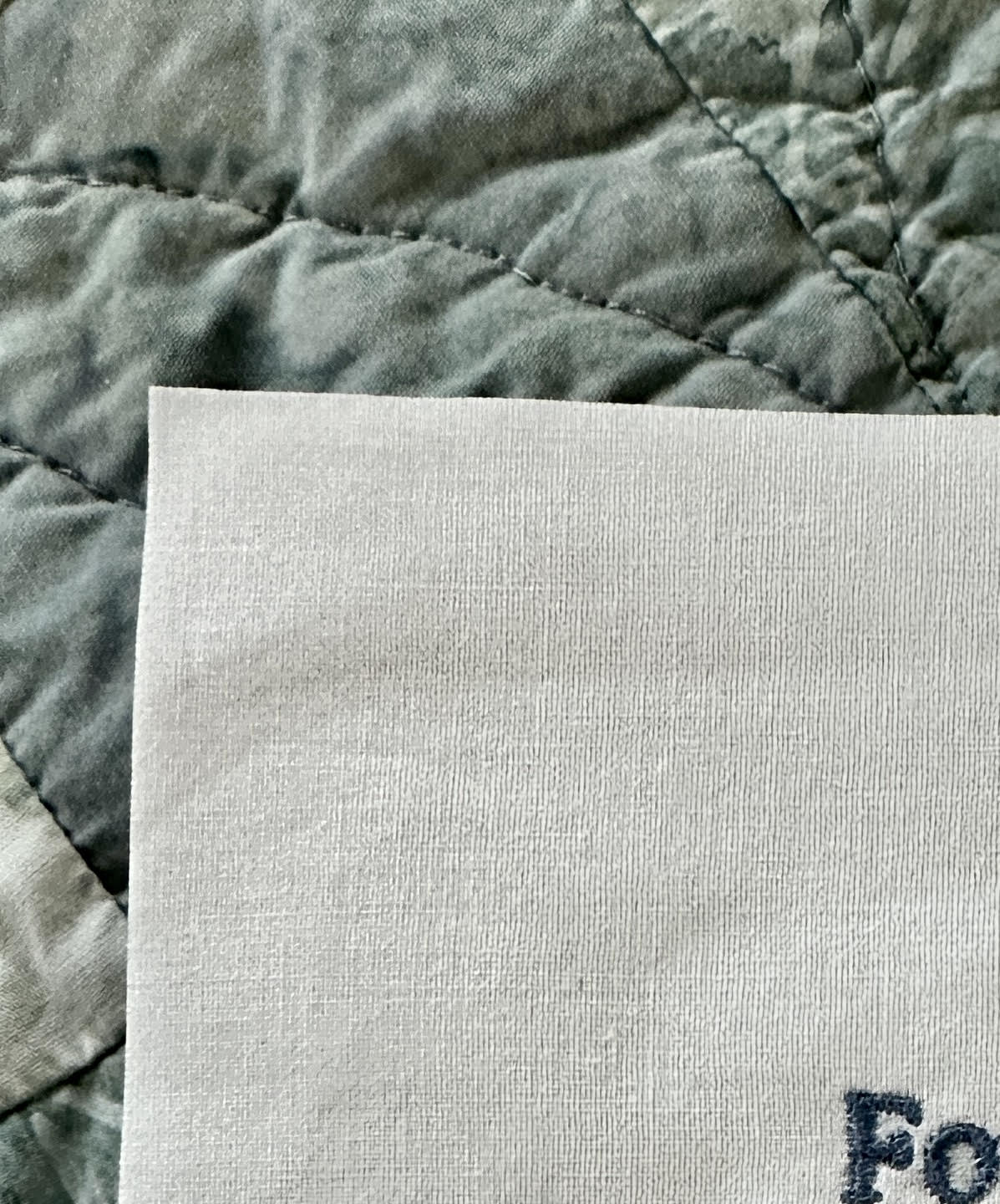 Close-up of a customized embroidered quilt label on 100% cotton fabric with unfinished edges, showcasing detailed stitching.
