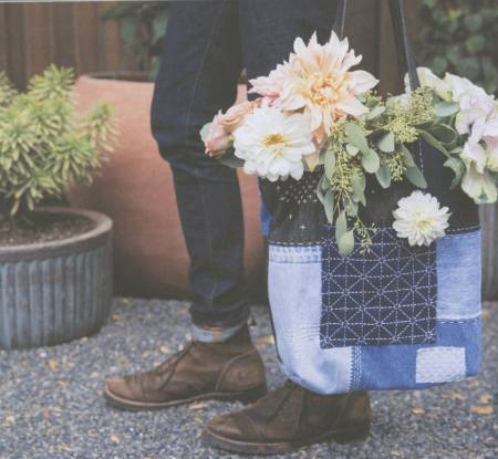 Person carrying a denim patchwork sashiko tote with flowers, showcasing Make and Mend Learning Sashiko techniques.