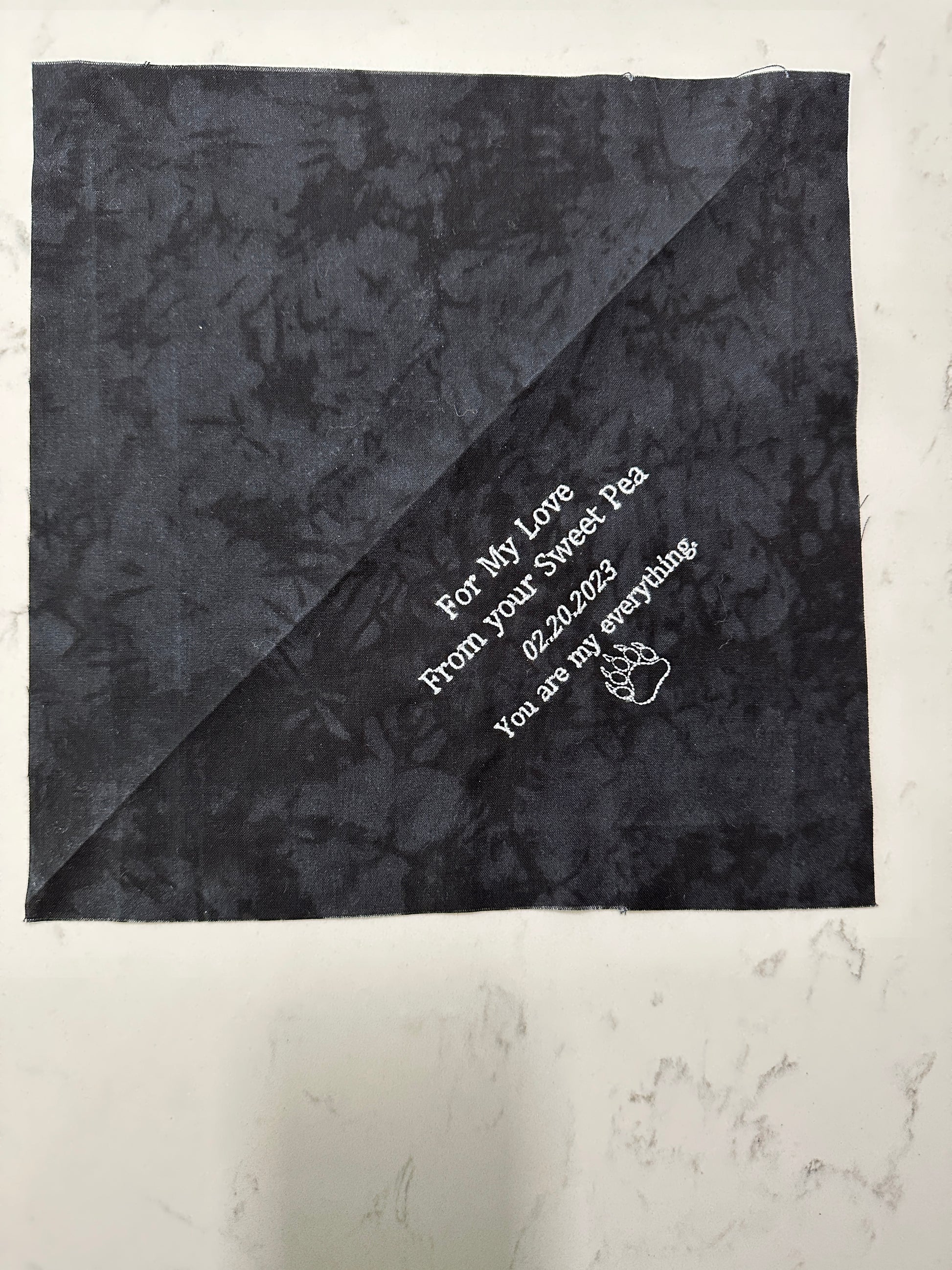 Custom embroidered quilt label with personalized message on dark cotton fabric, featuring a simple graphic design.