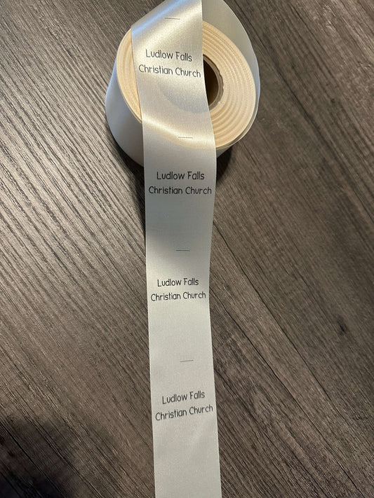 Roll of personalized satin ribbon labels with 'Ludlow Falls Christian Church' text, perfect for sewing and crafting.