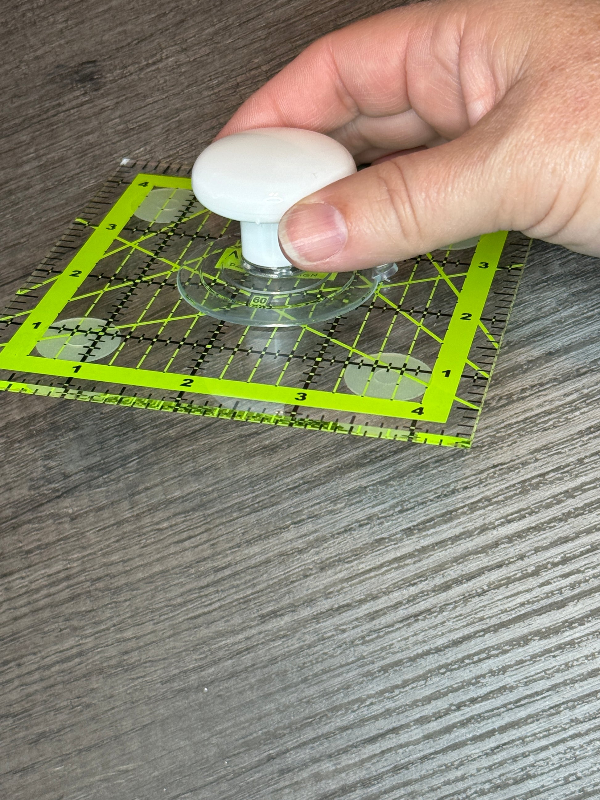 Hand using Ruler Knob Cottage Mills 8003 suction cup on a green sewing ruler for easy pickup and precise placement.