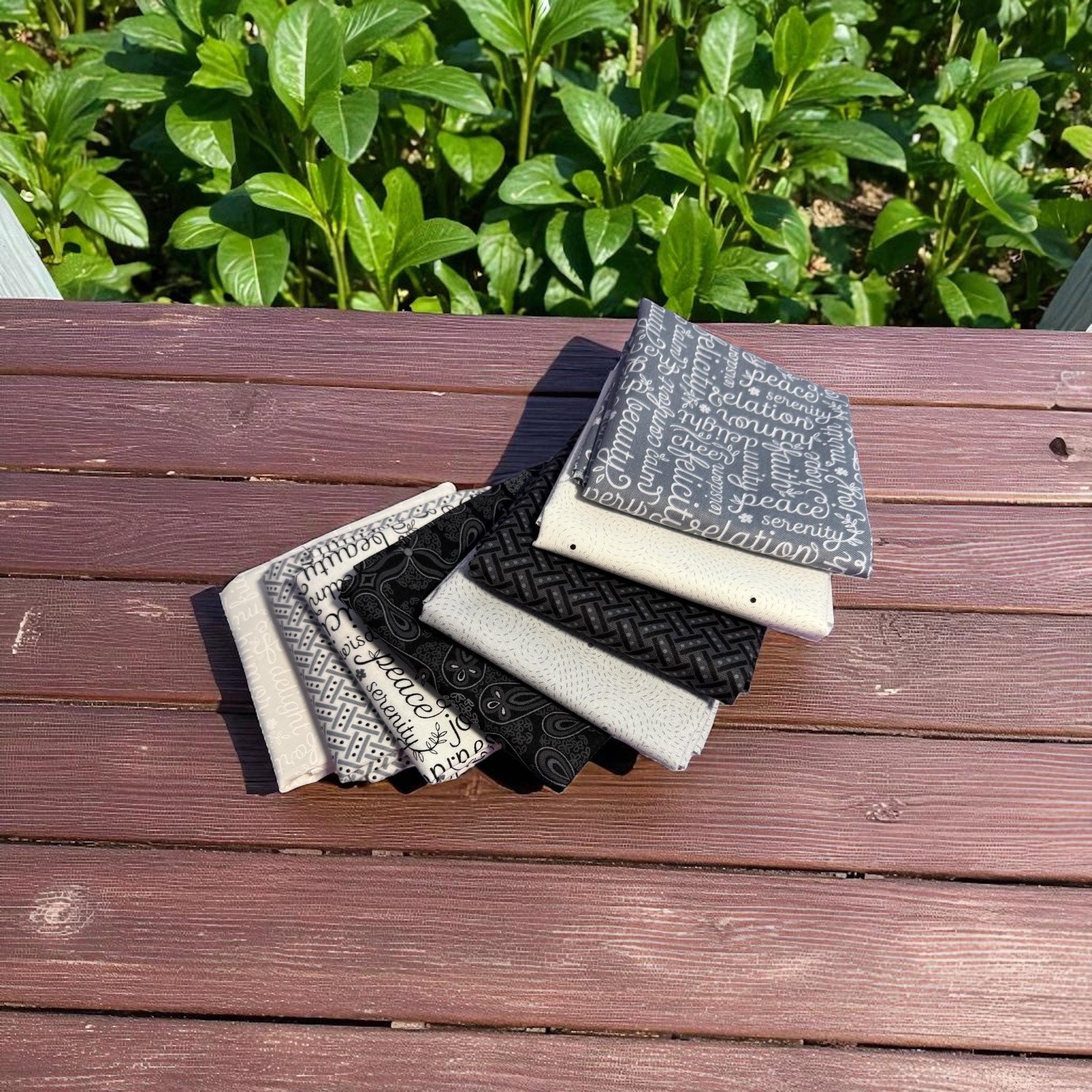 Cotton Fabric White Black Grey Benartex Botanica 8 Piece Bundle on wooden table, featuring black, gray, and white designs outdoors.