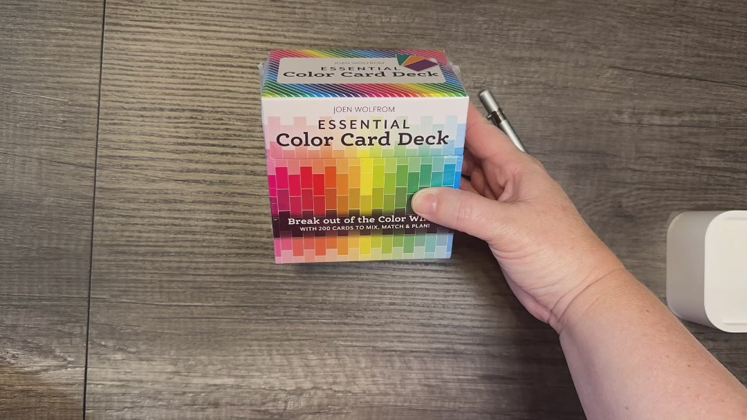 Close-up of a hand holding the Essential Color Card Deck, featuring a colorful box with coordinated color cards for confident color choices.